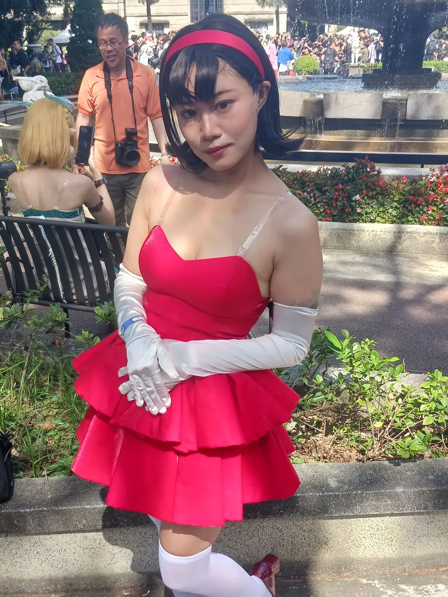 A cosplayer dressed as Mima Kirigoe from Perfect Blue in CHAM!'s pink tiered stage dress, red headband and long white gloves